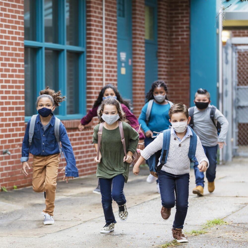 Students with face masks running outside school building