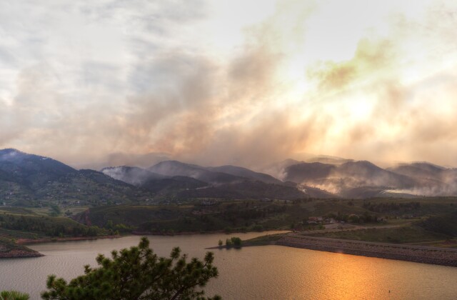Smoke from a wildfire billows across a mountaintop horizon. 
