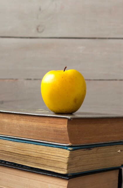 pile of old books and apple on wooden background