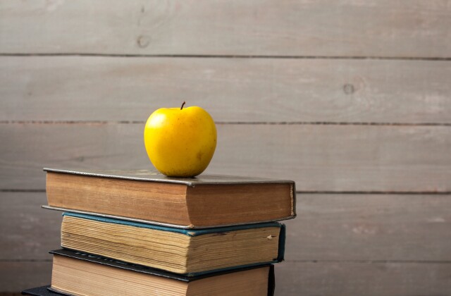 pile of old books and apple on wooden background
