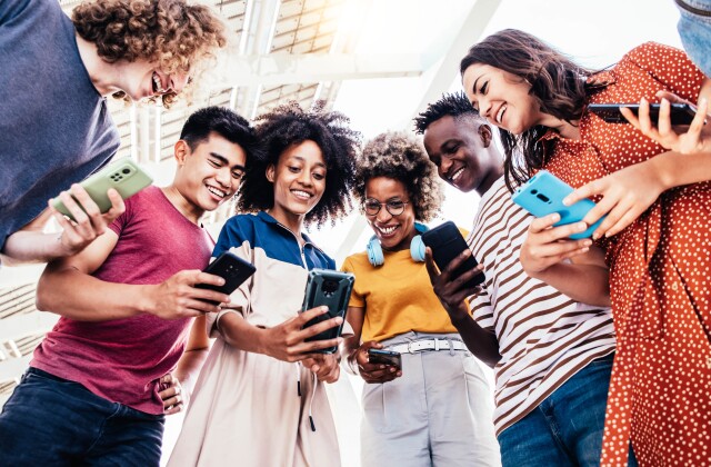 Diverse teenage students using digital smart phones mobile at college campus.