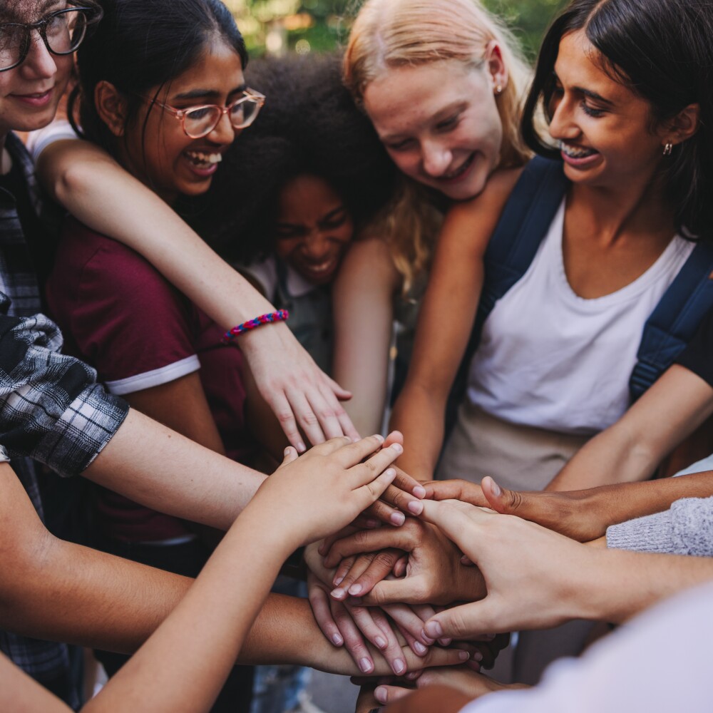 A group of young women gather in a circle and hold hands.