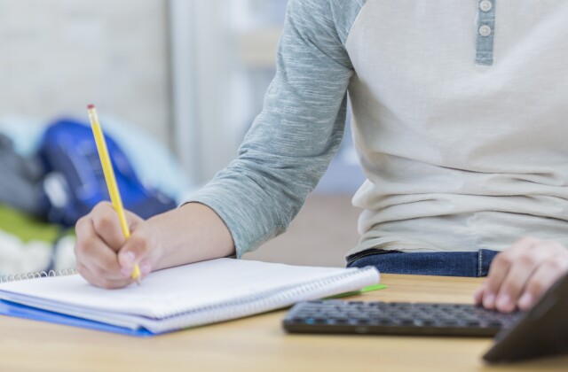 A student writes in a notepad while also working on a computer. 