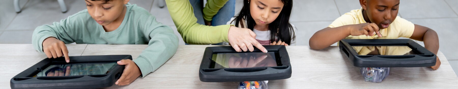 A teacher assists three students working on tablets. 