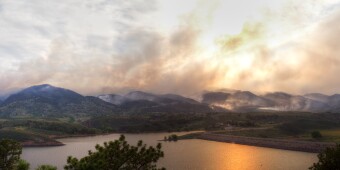 Smoke from a wildfire billows across a mountaintop horizon. 