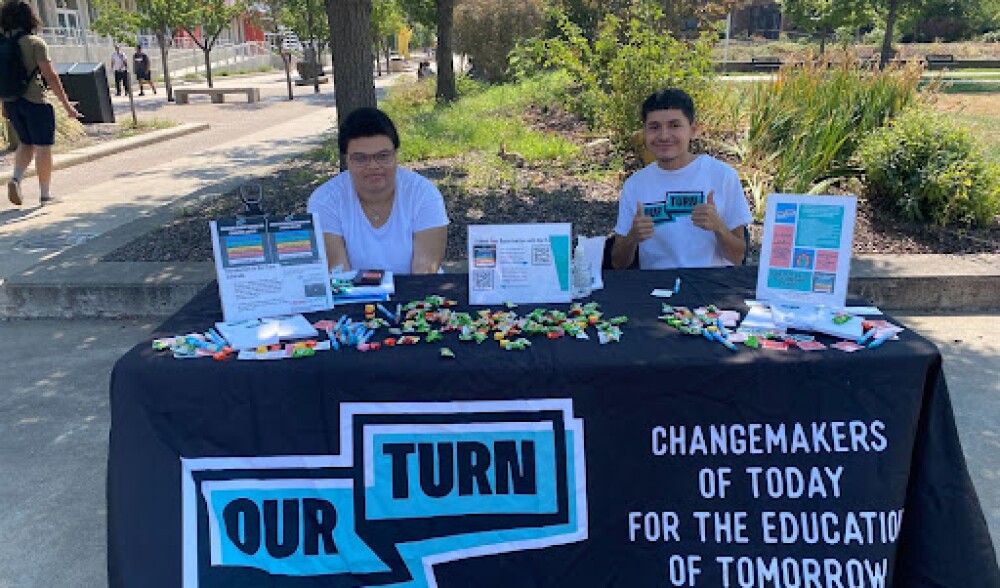 Two students sit at an informational table. 