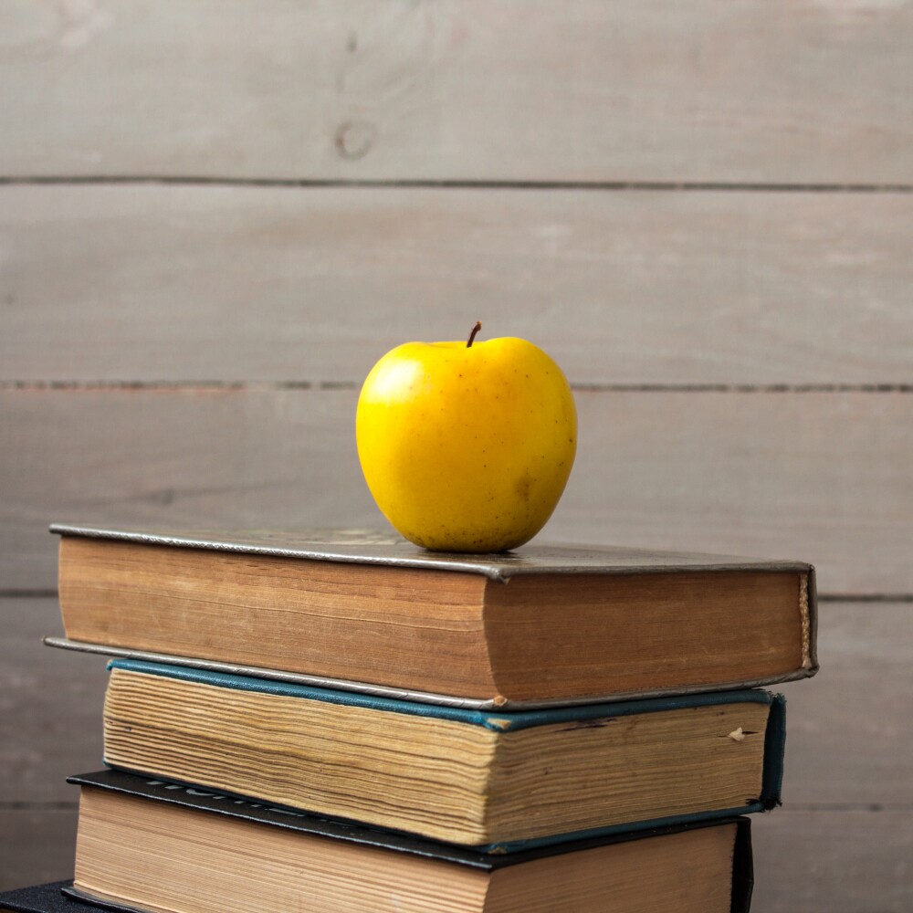 pile of old books and apple on wooden background