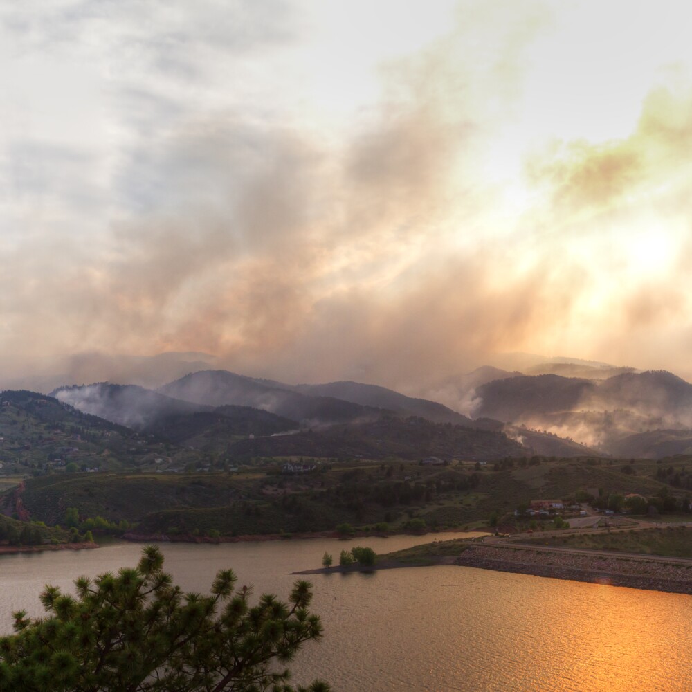 Smoke from a wildfire billows across a mountaintop horizon. 