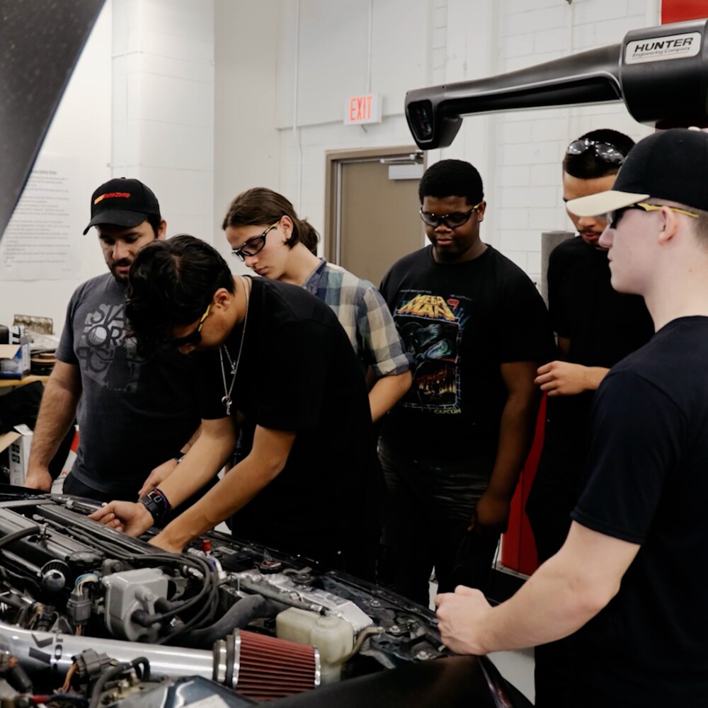 A group of young people work on fixing a car  engine.