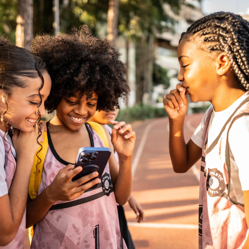 Three young students stand in a group looking at a smart phone. 
