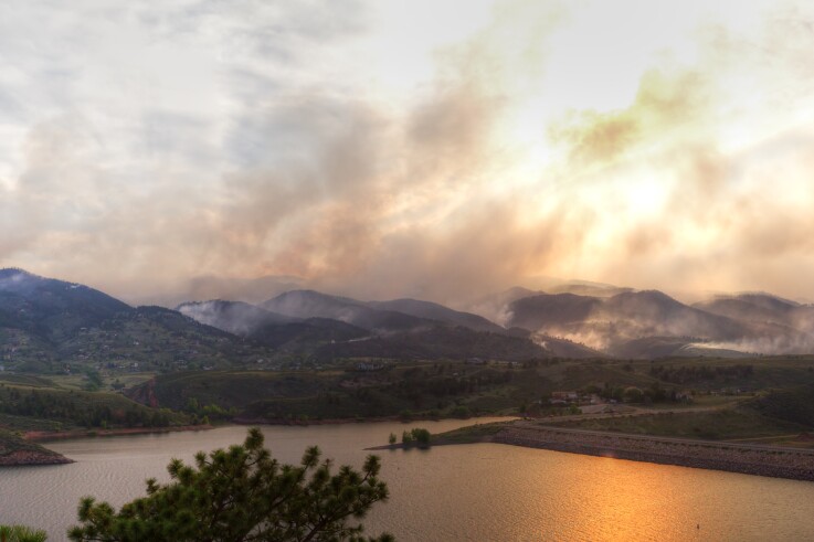 Smoke from a wildfire billows across a mountaintop horizon. 