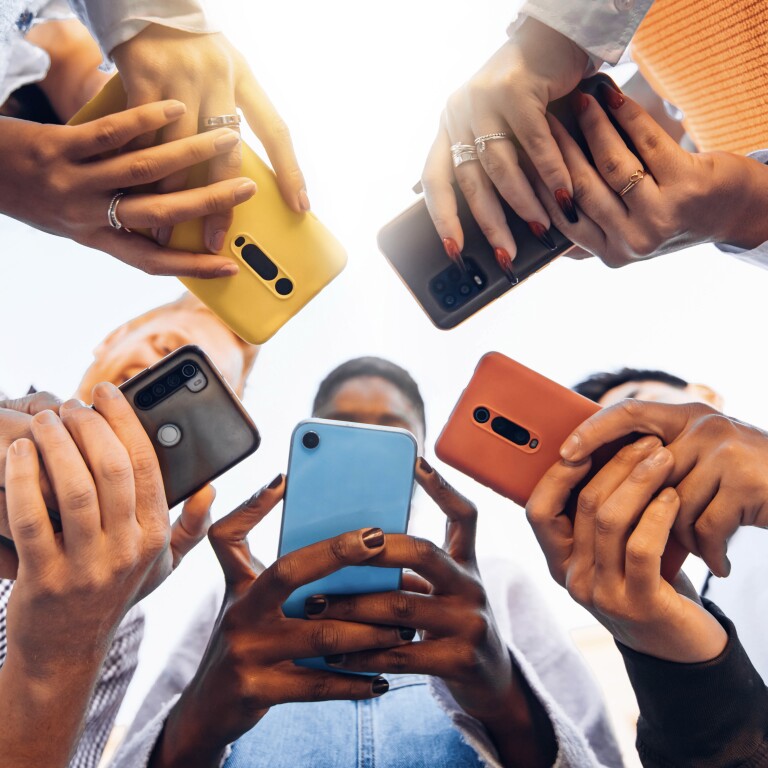 A group of Gen Z youth stand in a circle holding their phones. 