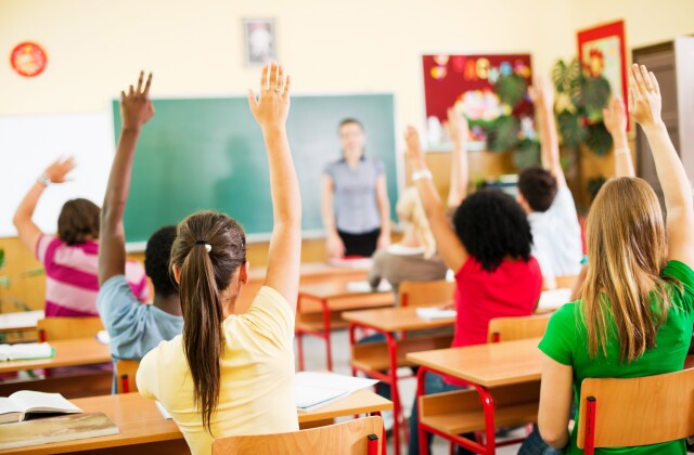 High School Students raise their hands in class. 