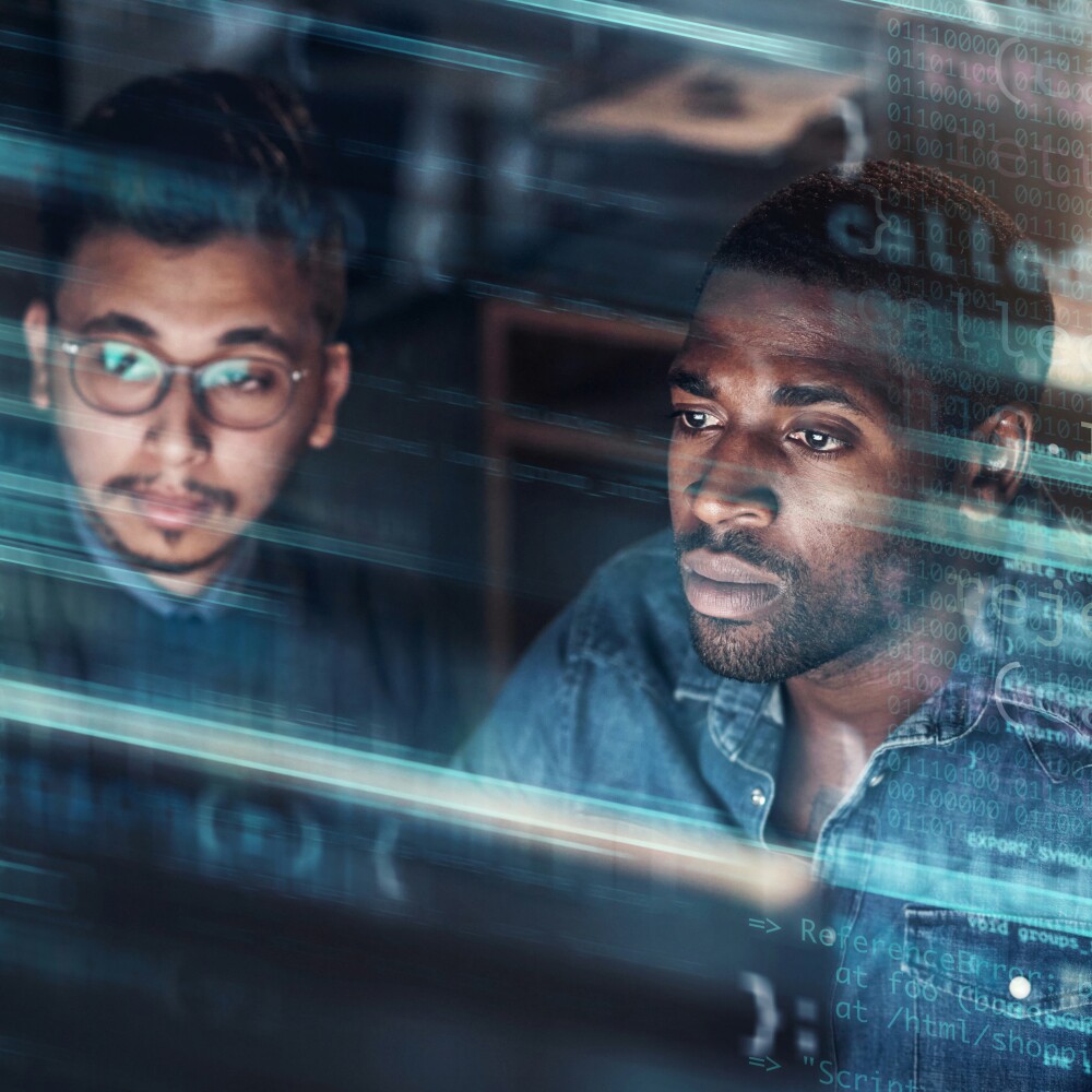 Two computer programmer work in an office superimposed over multiple lines of code.