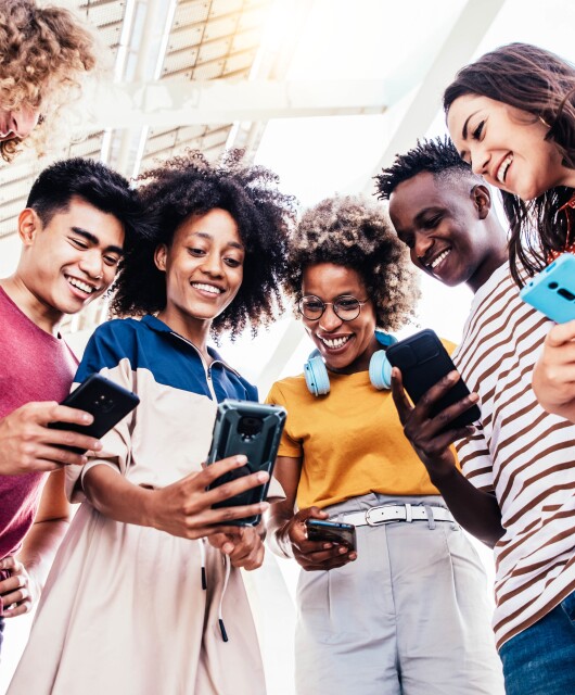 Diverse teenage students using digital smart phones mobile at college campus.