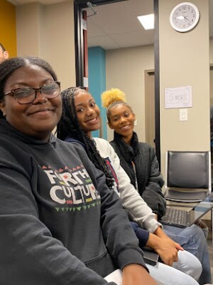 Three young women are seated in a waiting room. 