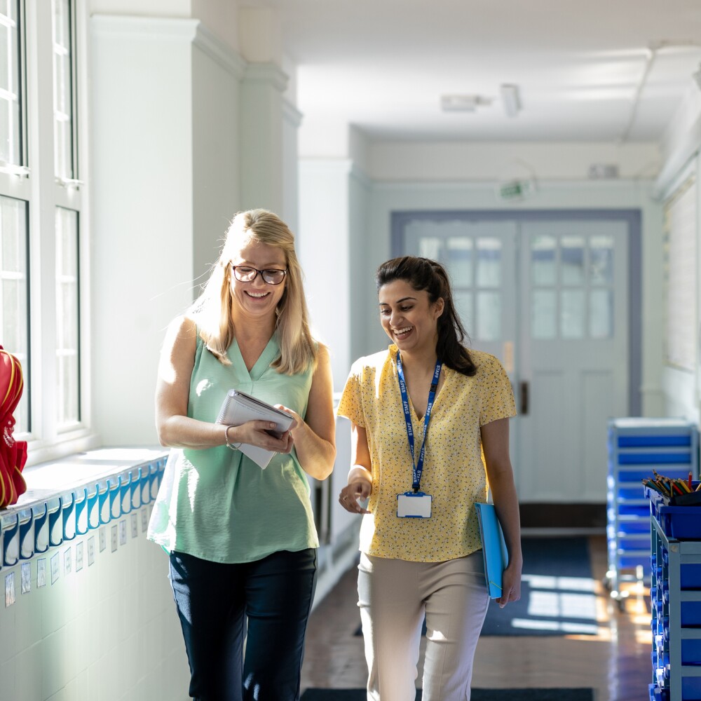 Two female teachers walk down a hallway. 