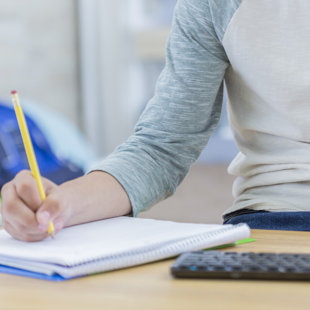 A student writes in a notepad while also working on a computer. 