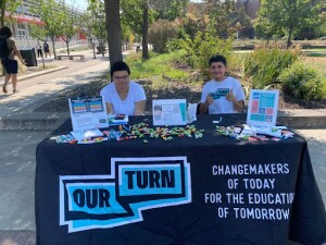 Two students sit at an informational table. 