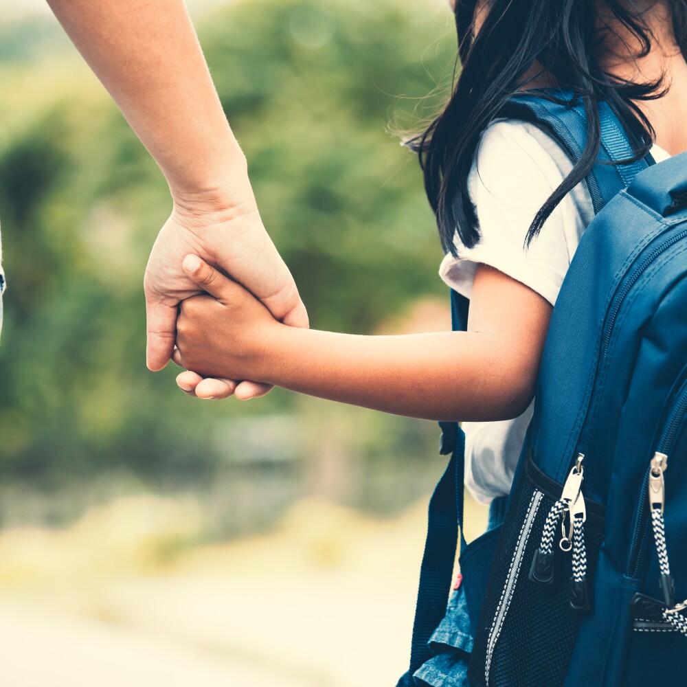 A parent holds her daughter's hand at school.