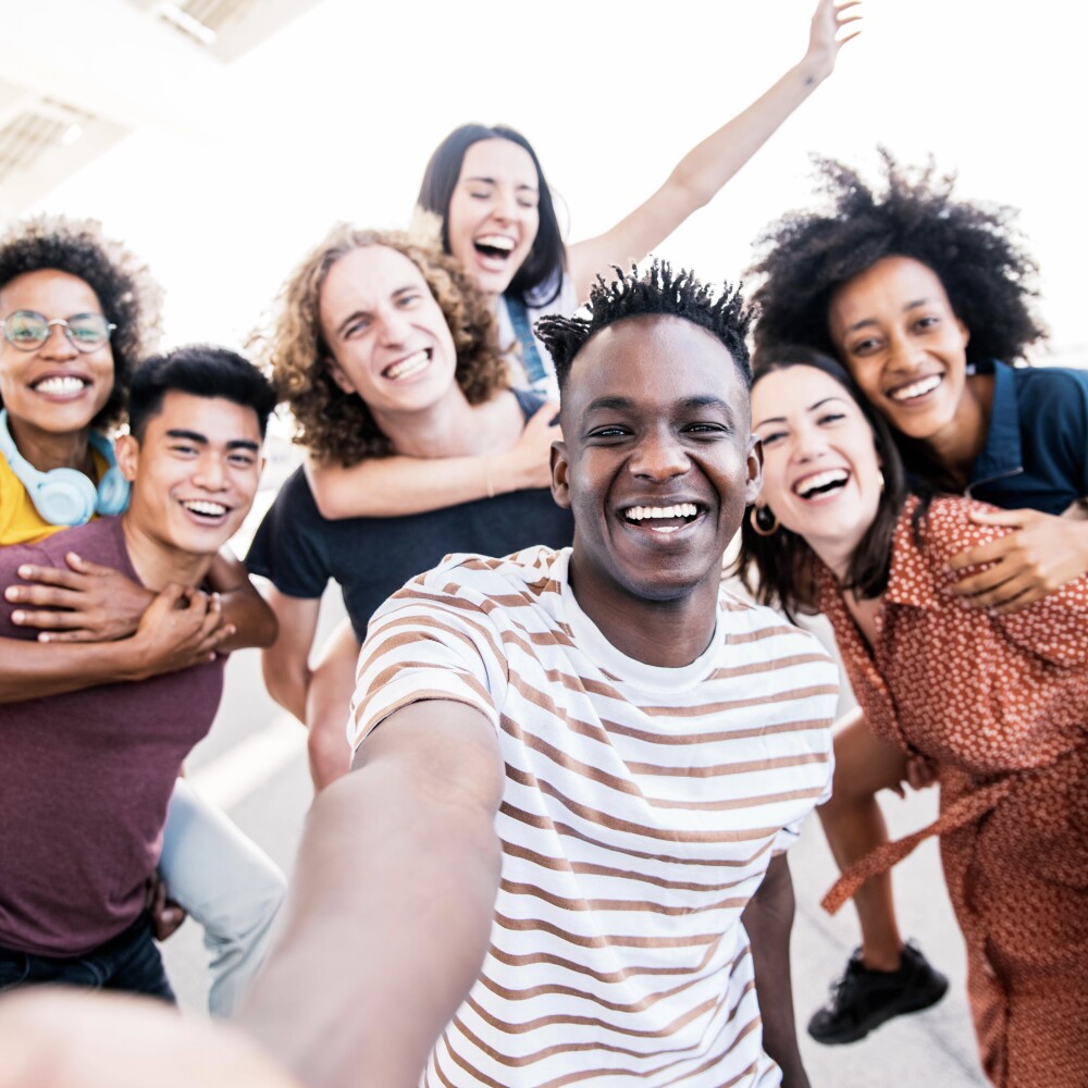 Multicultural happy friends having fun taking group selfie portrait on city street - Young diverse people celebrating laughing together outdoors - Happy lifestyle concept