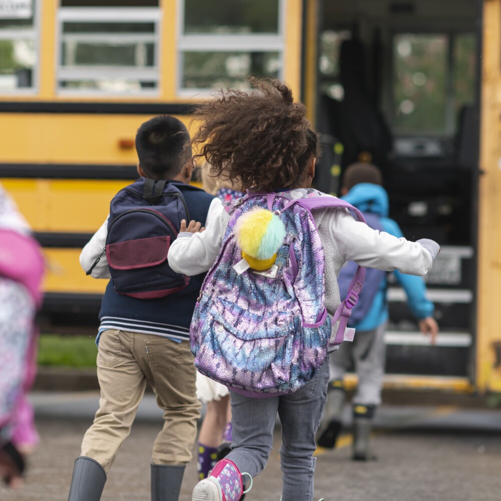 Diverse group of happy students running to school bus