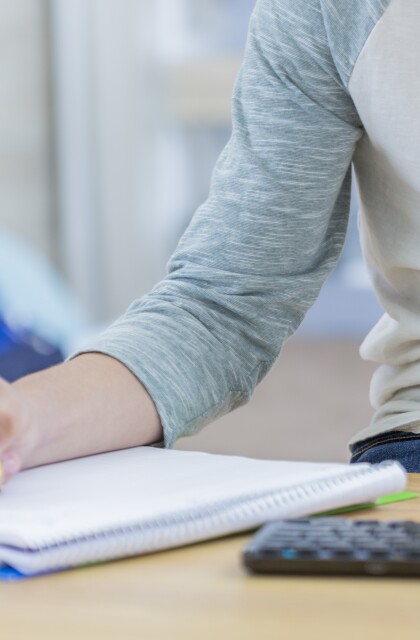 A student writes in a notepad while also working on a computer. 
