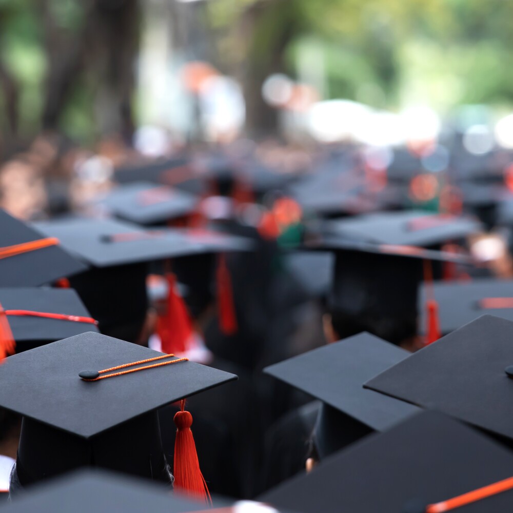 College students wear graduation caps with red tassles.  