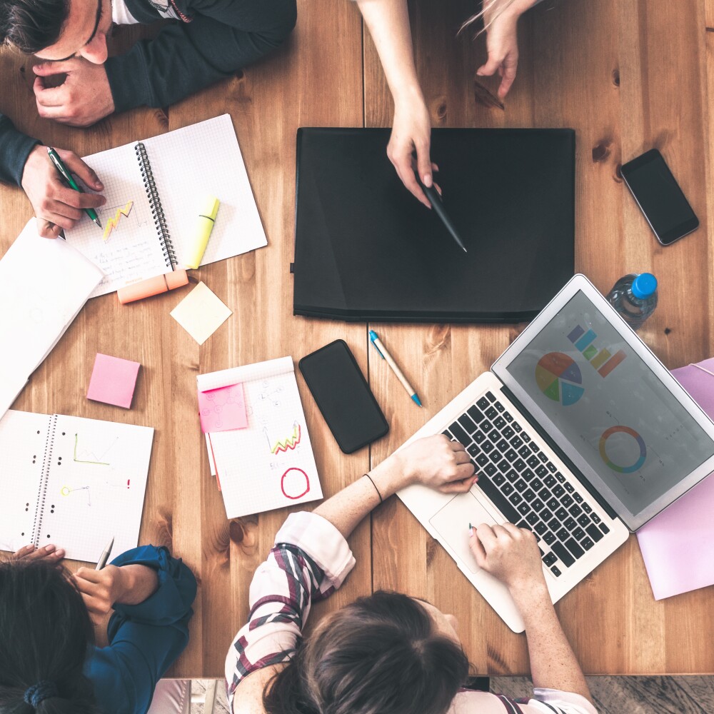A group of people sit a table and work on notepads and computers.