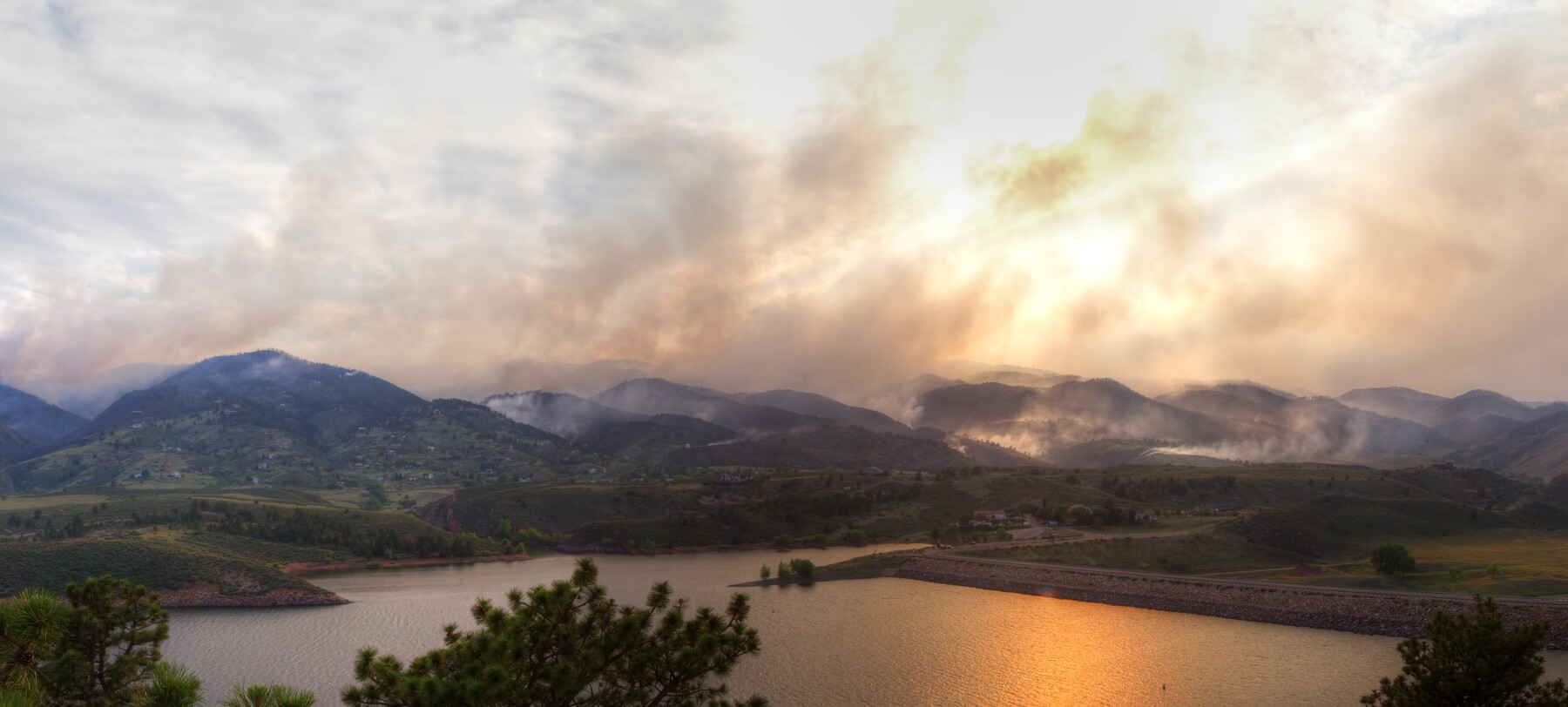 Smoke from a wildfire billows across a mountaintop horizon. 