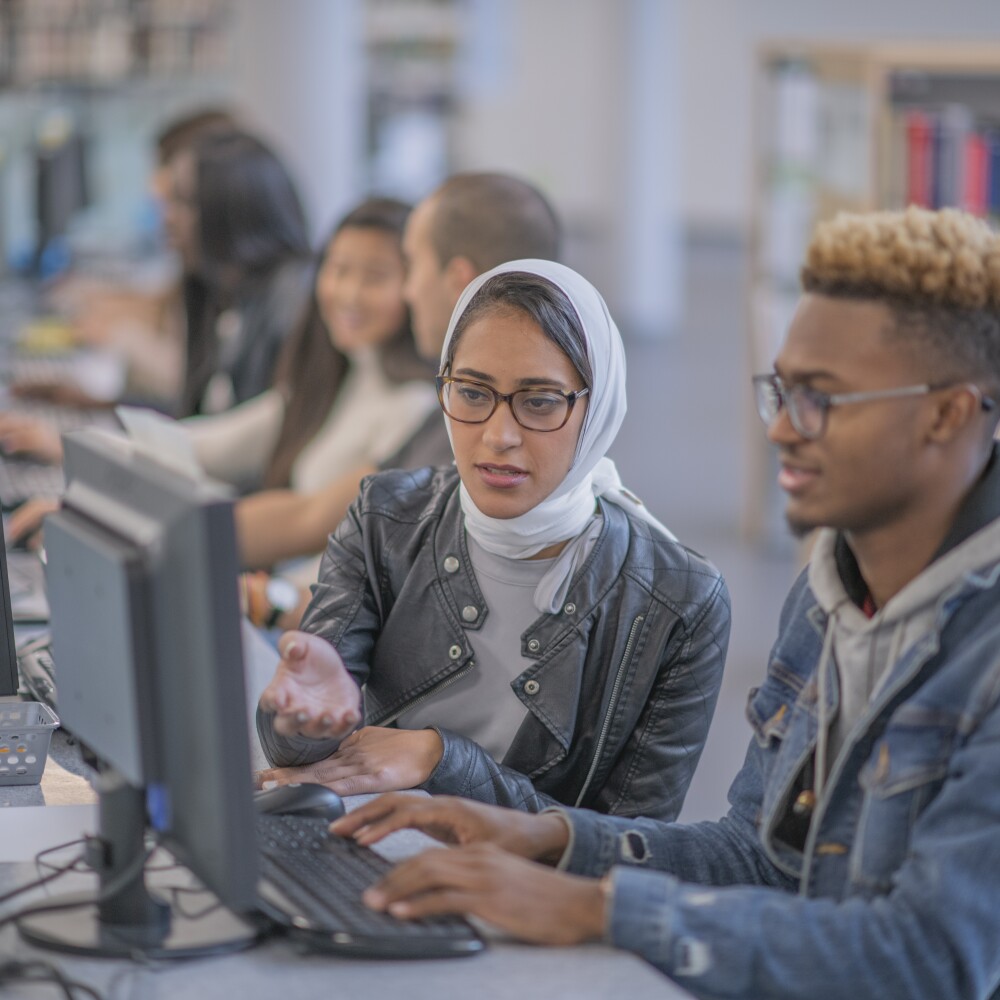 Students work on a row of computers in a classroom.