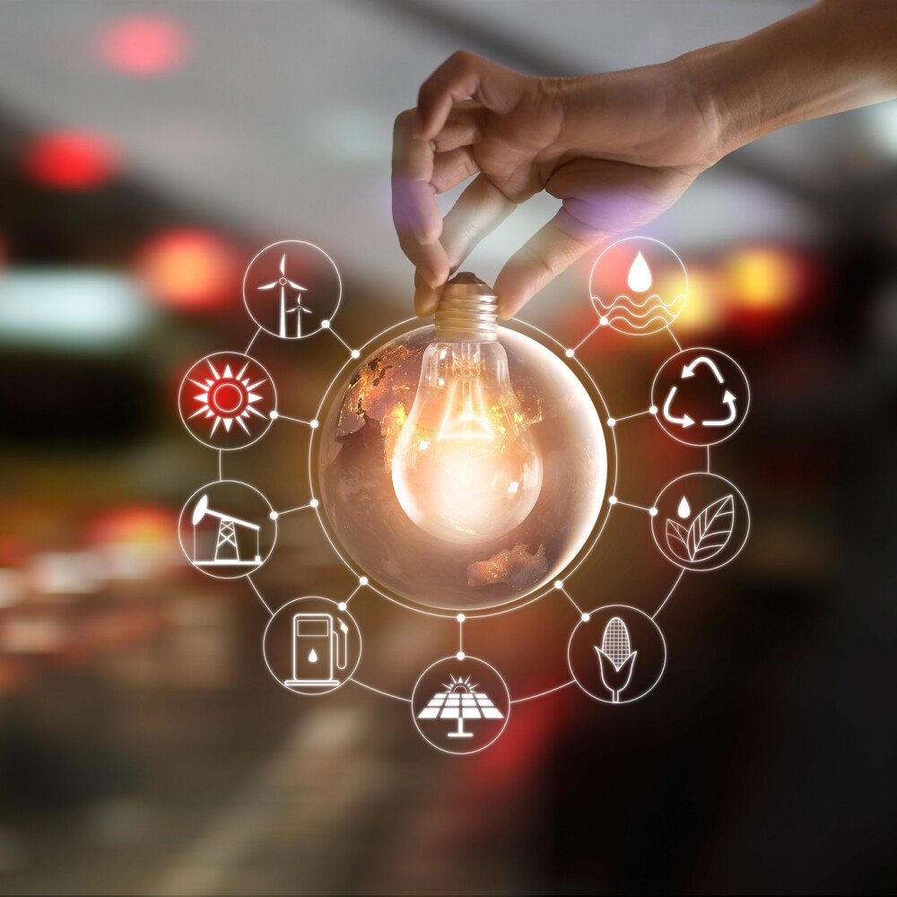 Hand holding light bulb in front of global show the world's consumption with icons energy sources for renewable, sustainable development. Ecology and environment concept.